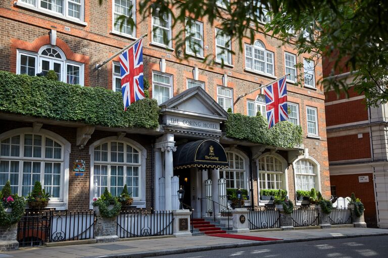 The front of the hotel on Beeston Place, with Union flags, climbing greenery, a canopied entrance and a red carpet, The Goring