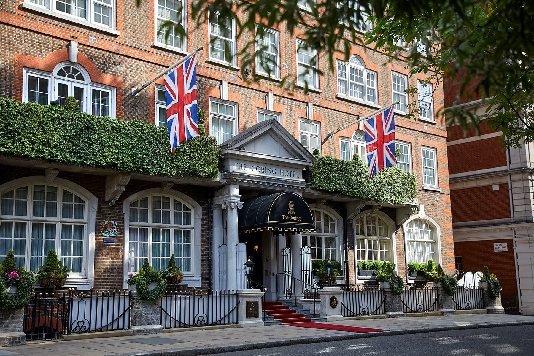 The front of the hotel on Beeston Place, with Union flags, climbing greenery, a canopied entrance and a red carpet, The Goring