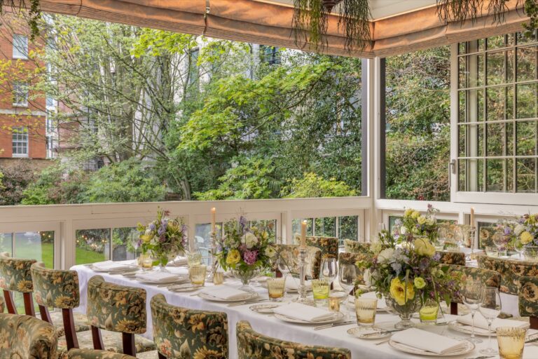 A long table dressed with wildflowers on The Veranda, its windows open to the garden trees, The Goring