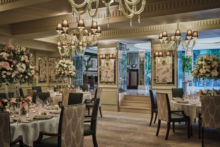 The Garden Room set with round tables, tall flower arrangements and glass chandeliers, The Goring