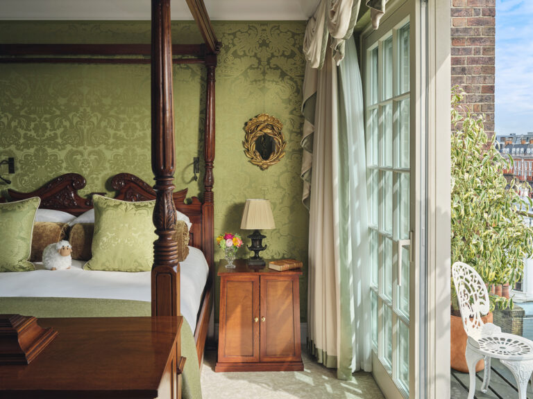 A four-poster bed against green silk walls, with glass doors to a terrace, The Goring