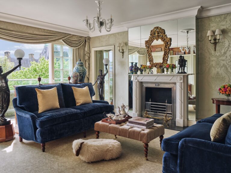 A living room with blue velvet sofas, a marble fireplace, a gilt mirror and a terrace window, The Goring
