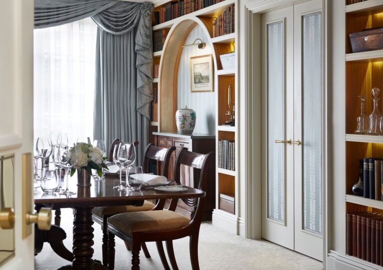 A dining table in a suite room lined with bookshelves and tall curtained windows, The Goring