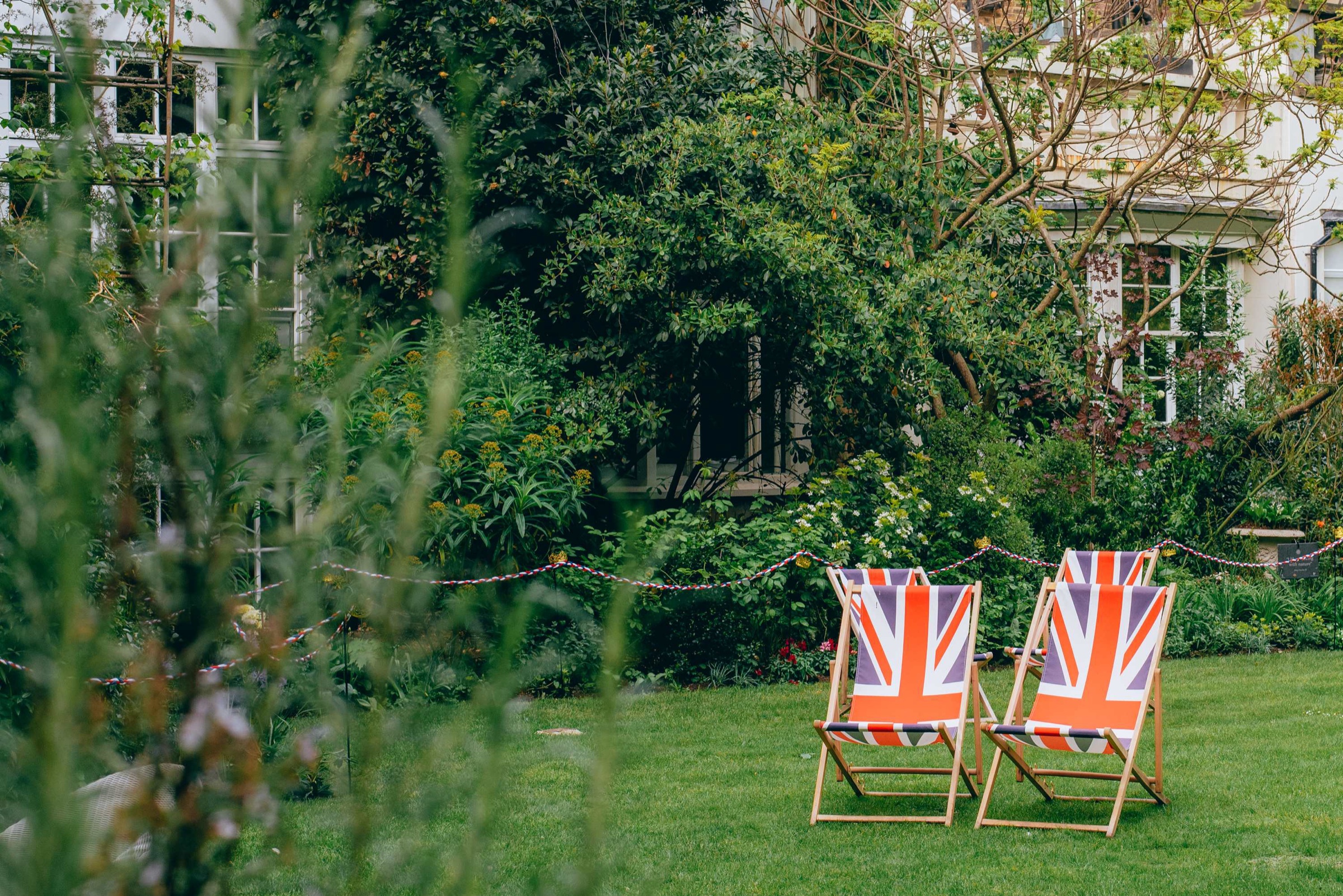 Two Union flag deckchairs on the lawn among trees and shrubs, The Goring