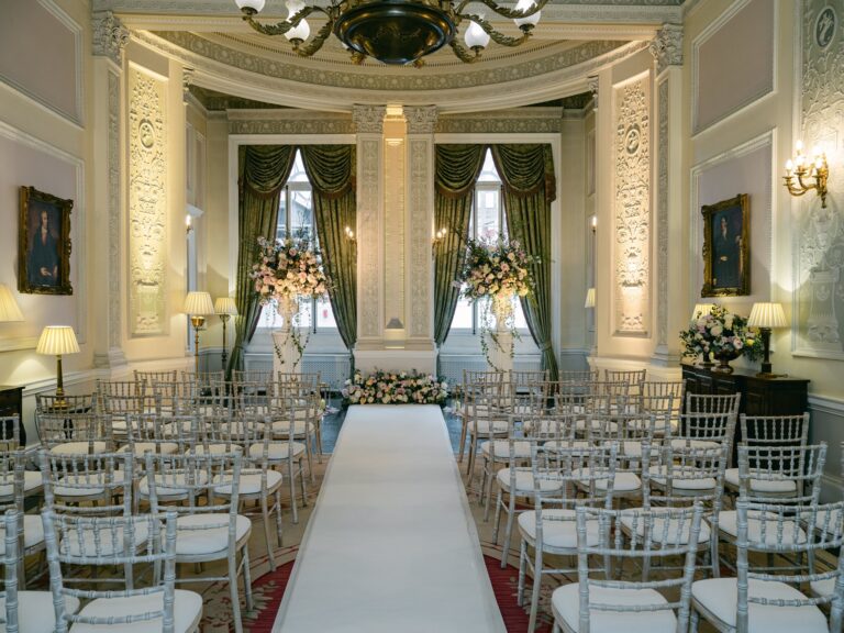 The Adam Room set for a ceremony, with a white aisle between rows of chairs and flowers by the windows, The Lansdowne Club