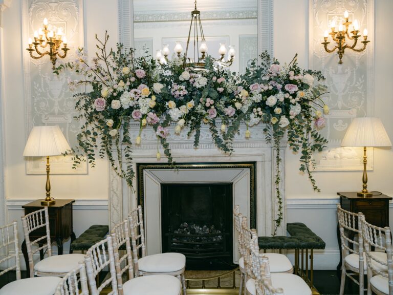 A marble fireplace dressed with roses and trailing greenery between two lamps, The Lansdowne Club