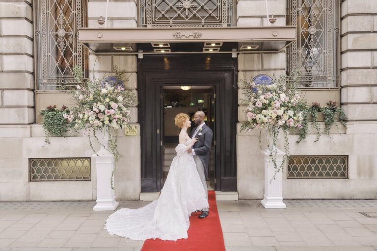 A couple at the Club entrance on a red carpet, with flower arrangements either side of the door, The Lansdowne Club