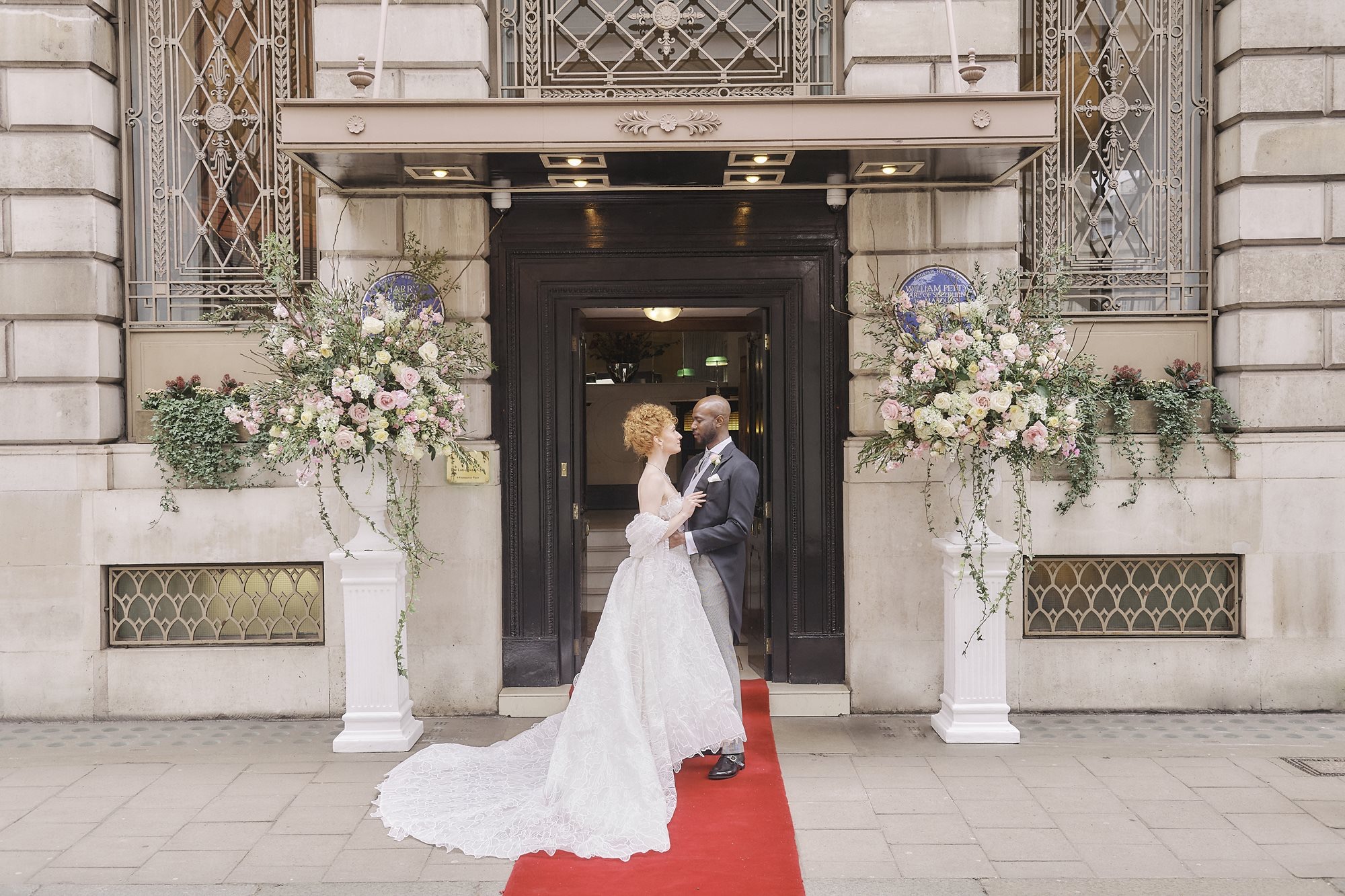A couple at the Club entrance on a red carpet, with flower arrangements either side of the door, The Lansdowne Club