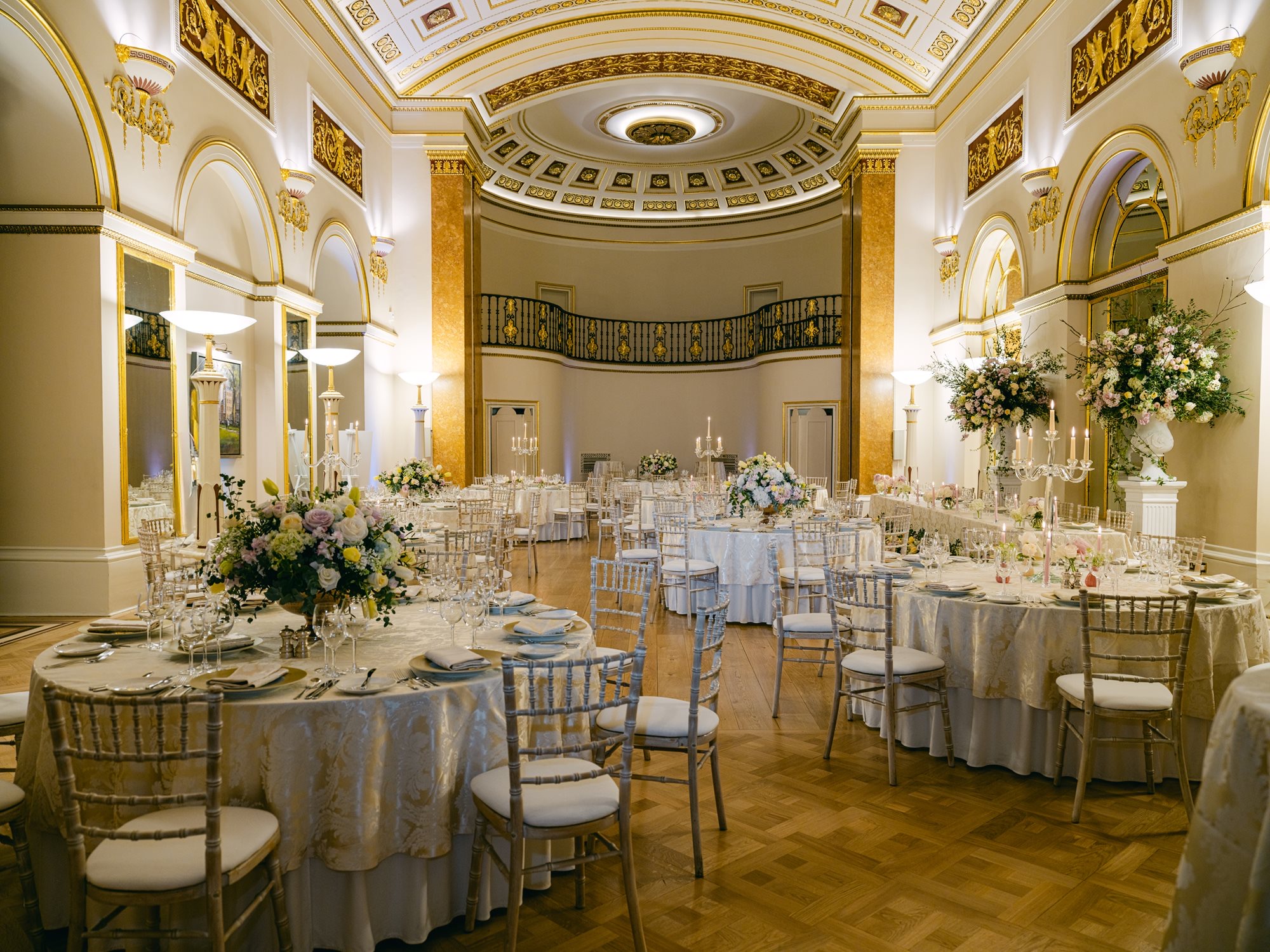 The Ballroom laid with round tables, candelabra and flowers beneath its vaulted ceiling and gallery, The Lansdowne Club