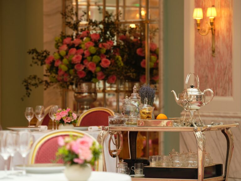 A silver trolley with a teapot and glasses beside a table with pink roses, The Ritz London