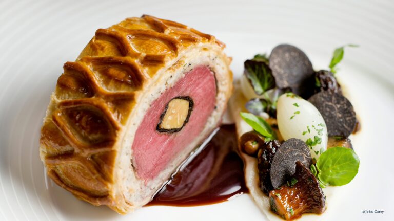 A sliced Wellington in pastry with truffle and garnish on a white plate, The Ritz London