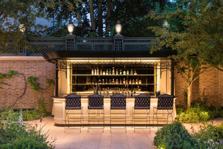 The Secret Garden bar lit at dusk, with stools in front of a bottle-lined counter, The Ritz London