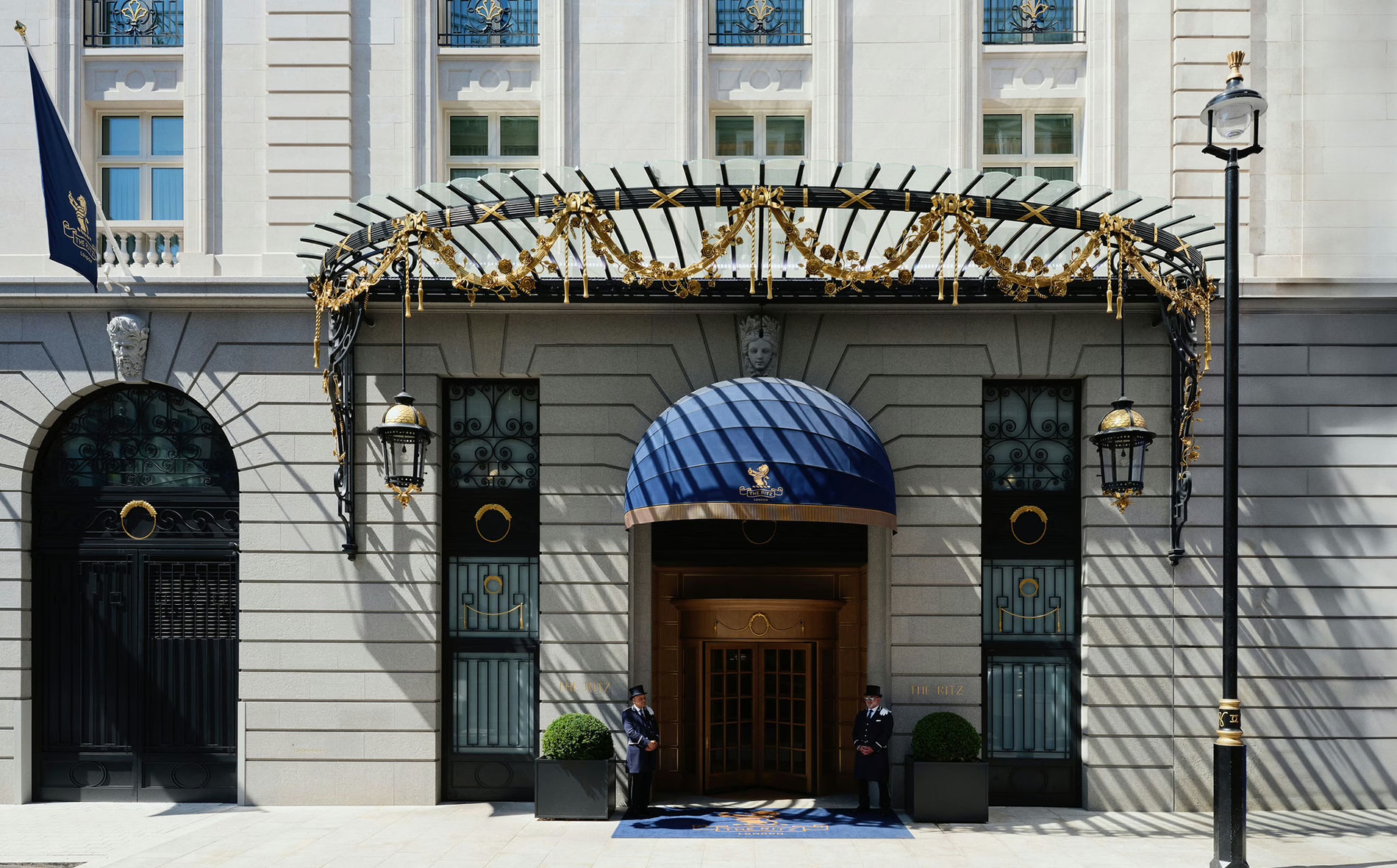 The hotel entrance under an iron and glass canopy, with a blue awning over the door, The Ritz London