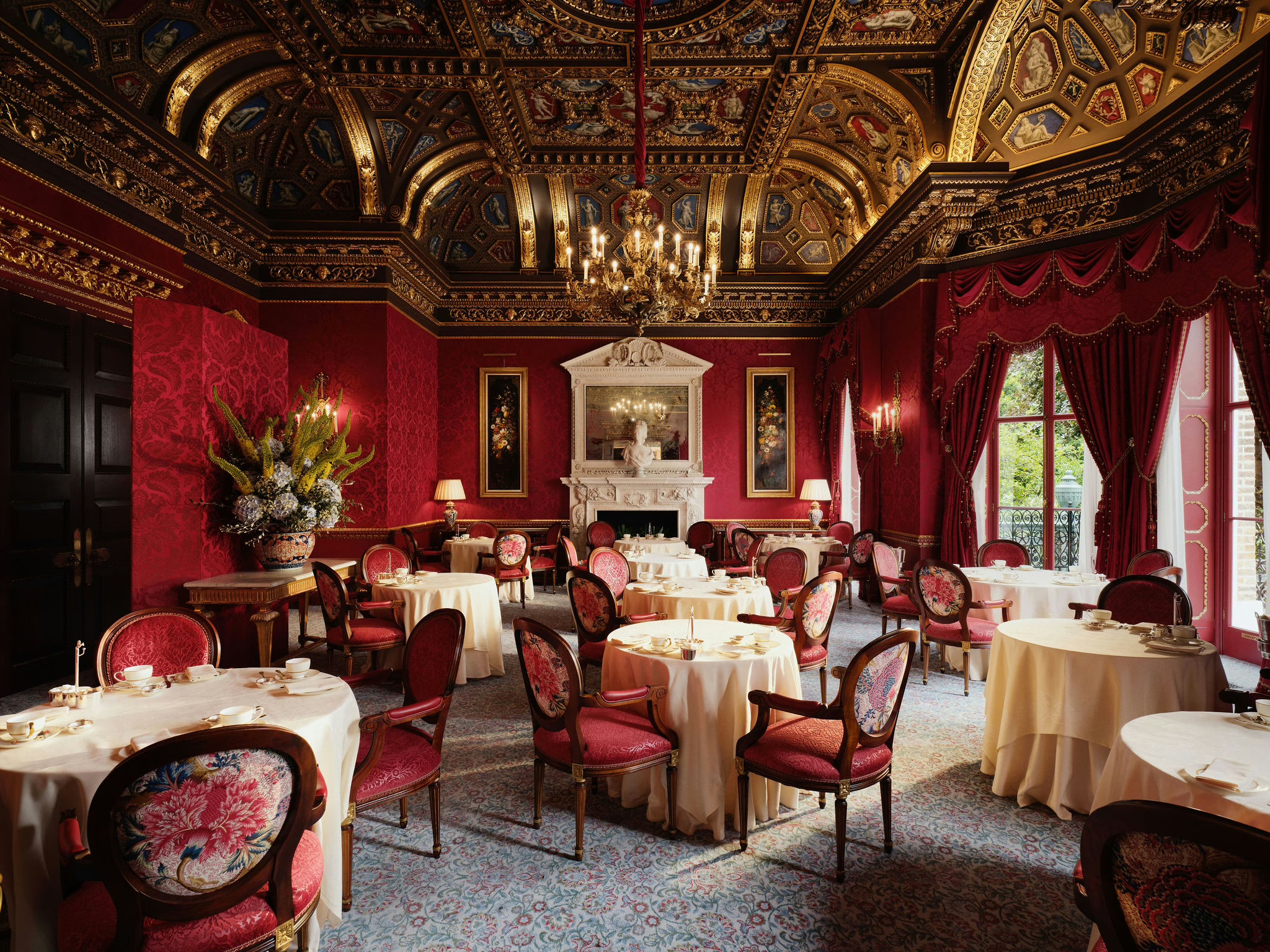 The William Kent Room laid with round tables and red chairs beneath a gilded, painted ceiling, The Ritz London