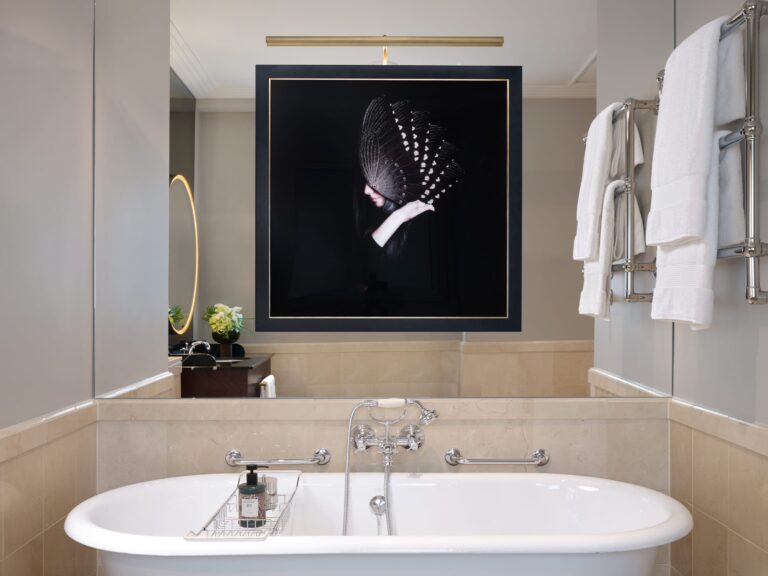 A marble bathroom with a freestanding bath and a framed artwork above it, The Savoy