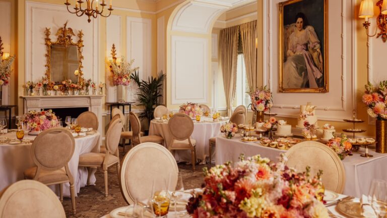 Tables dressed with pink and orange flowers in a private dining room with a gilt mirror and fireplace, The Savoy