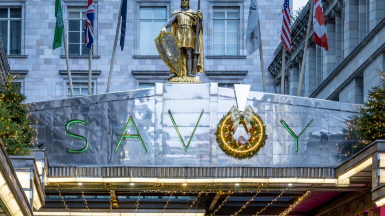 The steel canopy over the Savoy Court entrance, with the gilded statue above it and flags on the facade, The Savoy