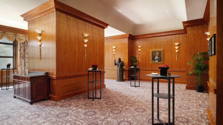 A wood-panelled private room with a bronze bust, a framed portrait and cocktail tables, The Savoy