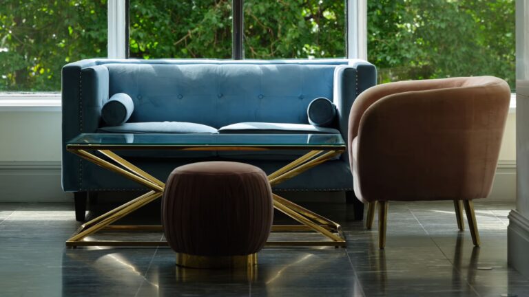 A blue velvet sofa and armchair by tall windows onto green trees, The Savoy