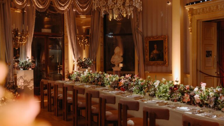 A long table dressed with flowers and candles beneath draped windows and a marble bust, The Wallace Collection
