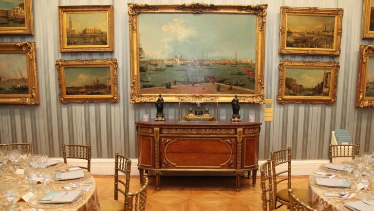 Round tables laid beside a gilt sideboard in a room hung with gilt-framed views of a city on the water, The Wallace Collection