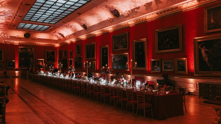 A long banquet table down a skylit gallery, lit in red for an evening celebration, The Wallace Collection