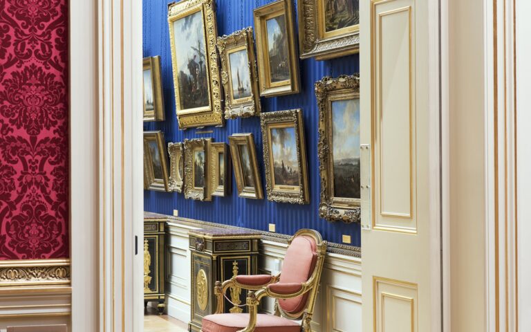 A doorway from a crimson room into a blue gallery hung with gilt-framed paintings, The Wallace Collection