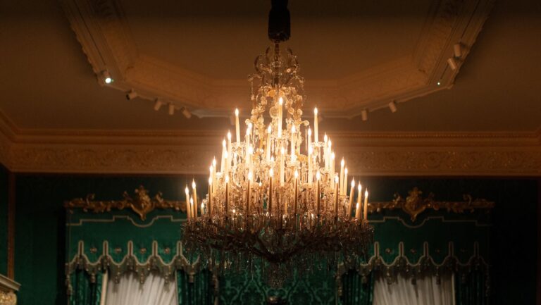 A lit crystal chandelier in a room with green silk walls and gilt mouldings, The Wallace Collection