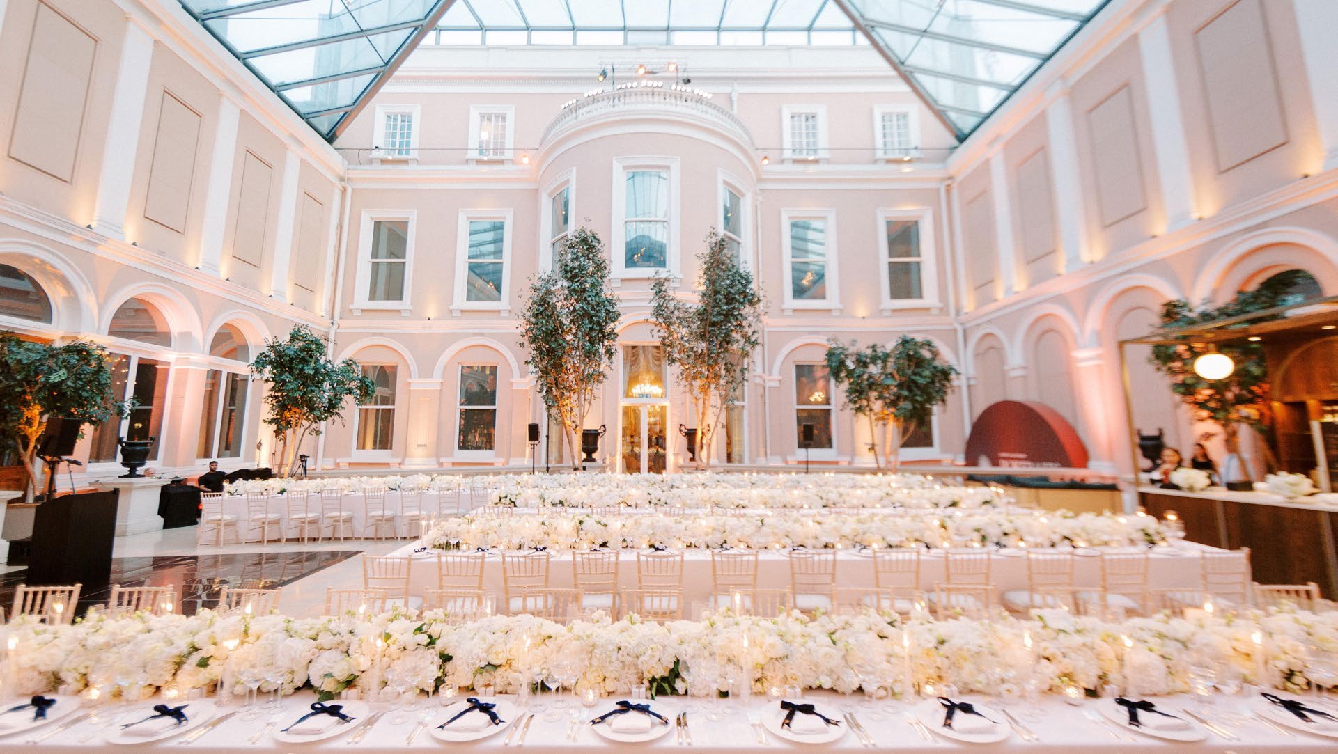 The glass-roofed Courtyard laid for dinner, with long tables banked with white flowers, The Wallace Collection