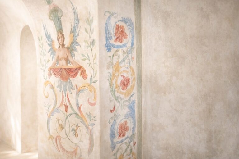 Restored painted fresco of a winged figure and floral scrolls on a pale plaster wall, Torre Collevento
