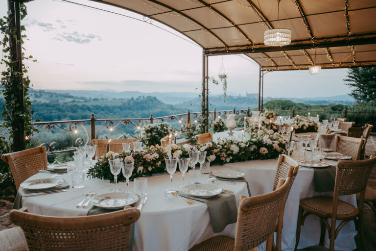 Round tables laid for a wedding dinner under the covered terrace, with the valley beyond the railing, Torre Collevento