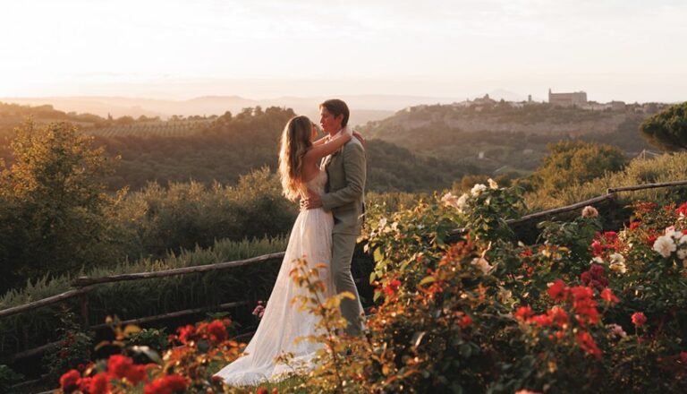A couple among red roses at the garden edge, with the hills and the town of Orvieto on the skyline, Torre Collevento