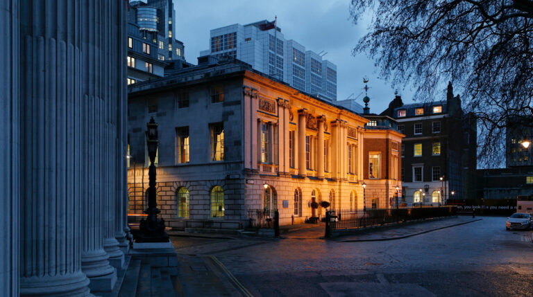 Trinity House lit at dusk, seen past the columns across Trinity Square, Trinity House on Tower Hill