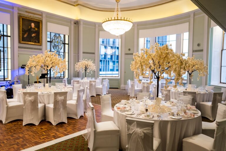 The Library dressed with blossom-tree centrepieces and white chair covers for an evening reception, Trinity House on Tower Hill