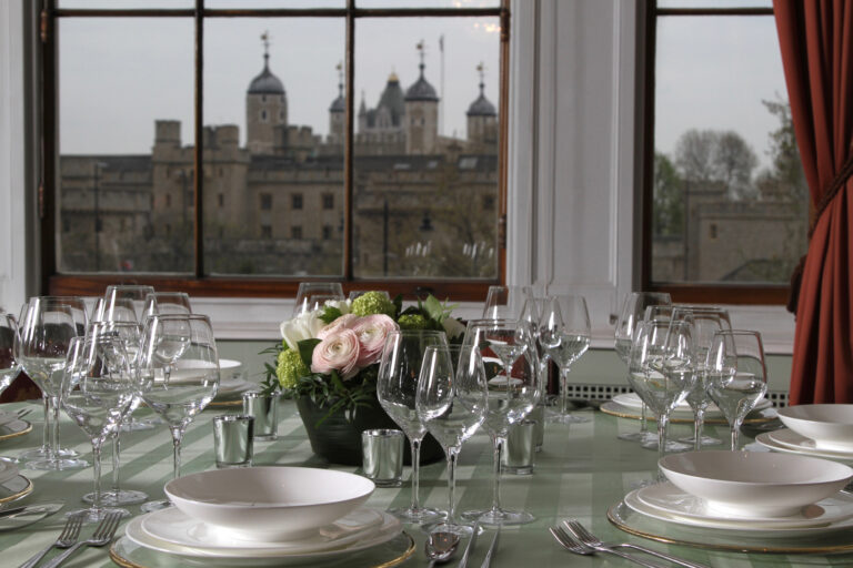 Glassware and flowers on a table set in front of a window facing the Tower of London, Trinity House on Tower Hill