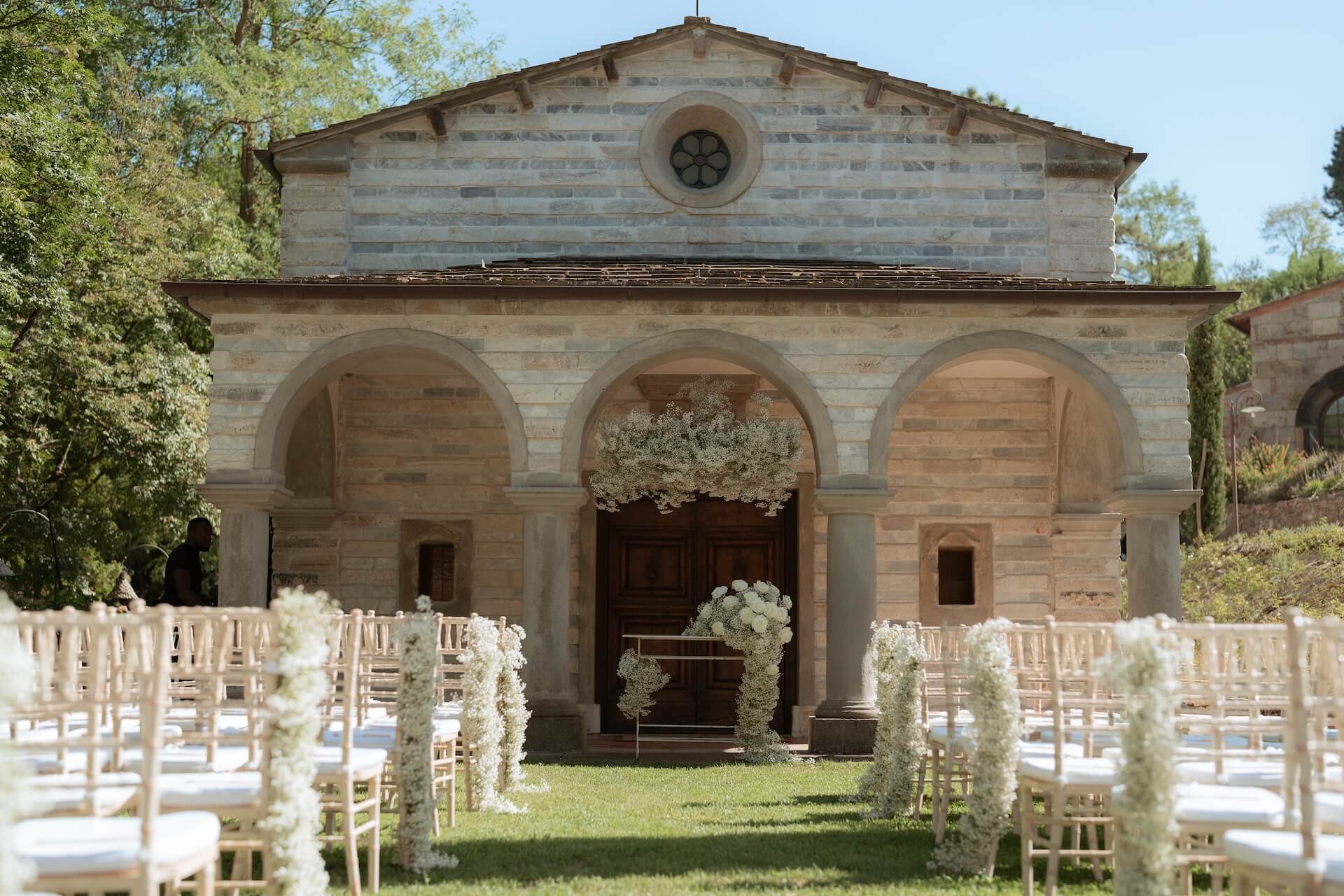The chapel of San Michele with its arched loggia, chairs set on the lawn for a ceremony, Valle di Badia