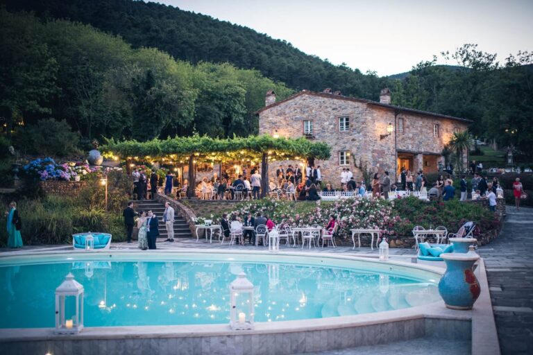 The pool at dusk, with guests under the lit pergola by a stone house, Valle di Badia