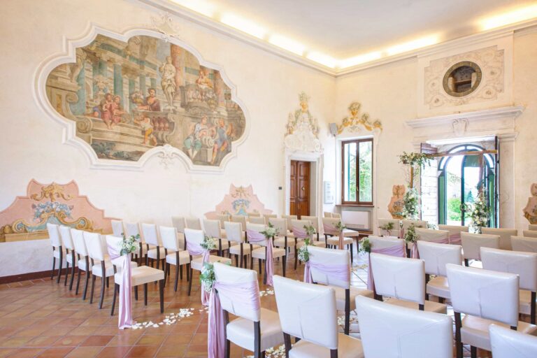 A frescoed hall with white chairs set in rows for an indoor ceremony, Villa Cariola
