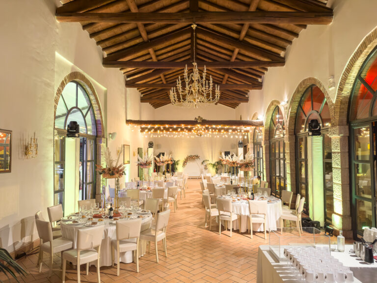 A hall with arched windows and a beamed ceiling, laid with round tables for a wedding dinner, Villa Cariola