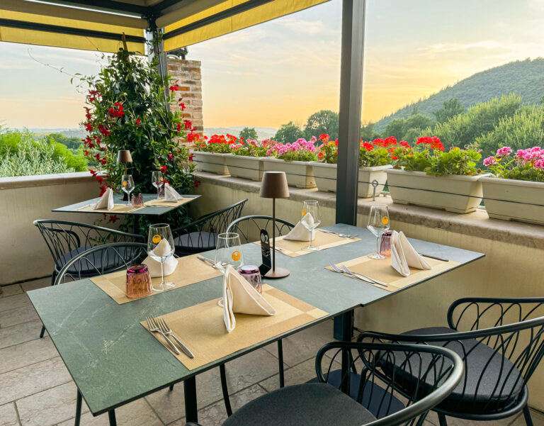 Tables on the restaurant terrace under a pergola, with flowers and the hills behind, Villa Cariola