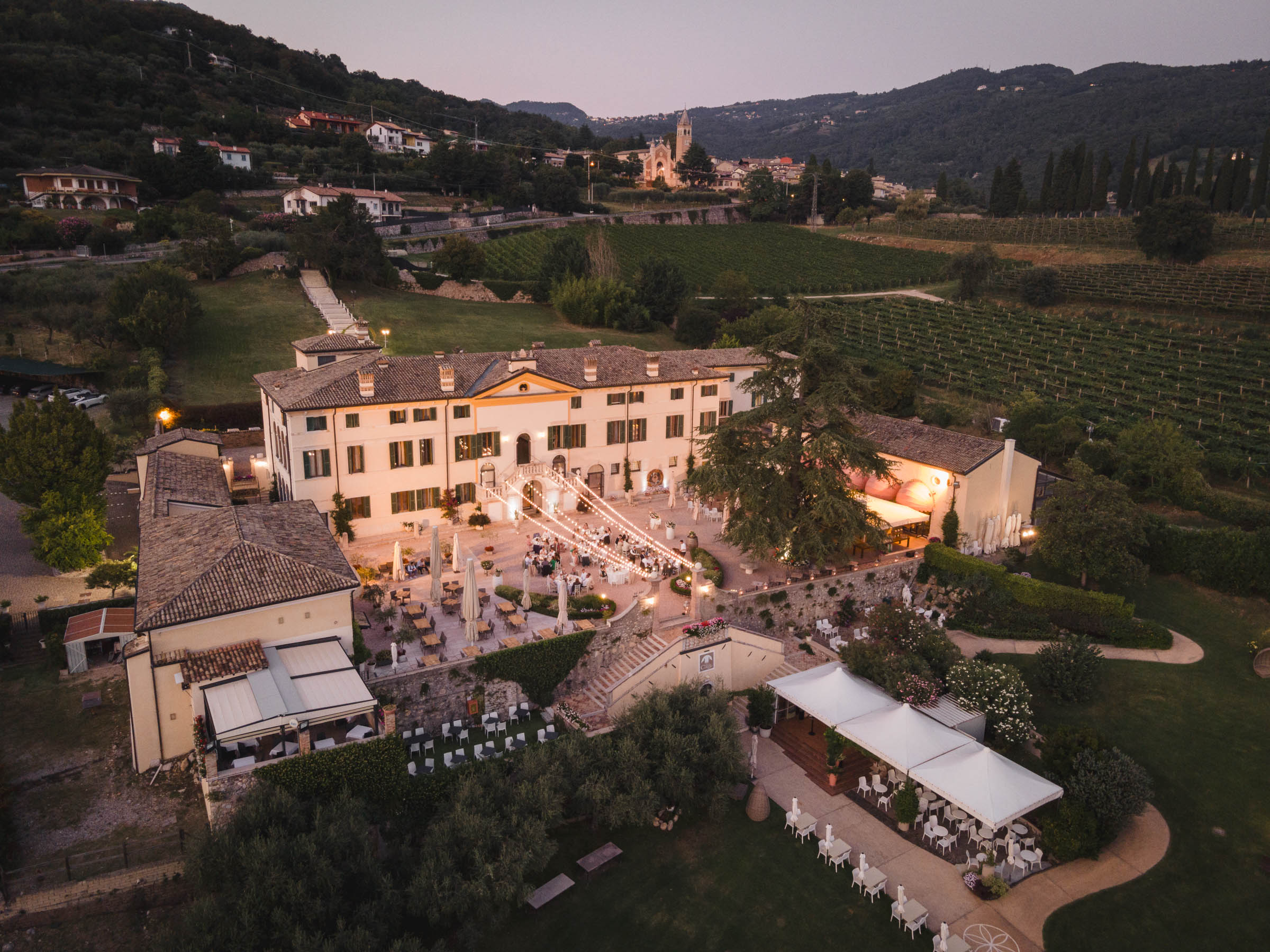 Villa Cariola from the air at dusk, with the courtyard lit and vineyards and hills behind, Villa Cariola