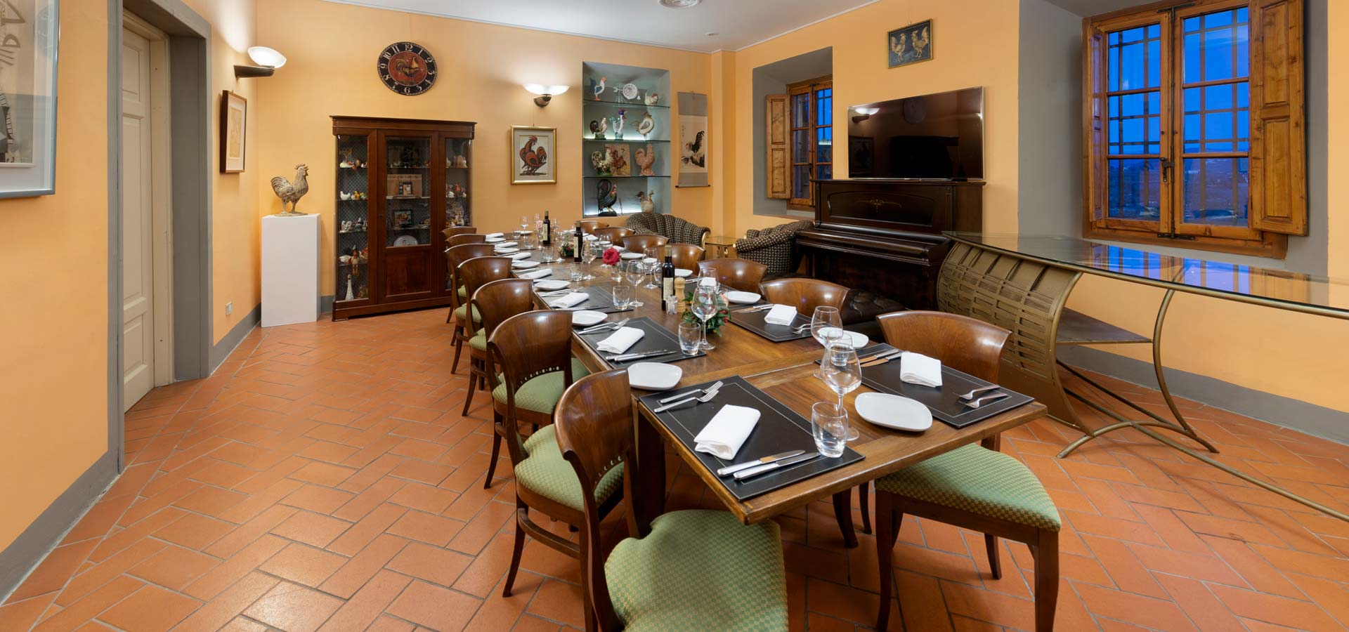 Dining room with a long laid table, terracotta floor and an upright piano at Villa Castiglione