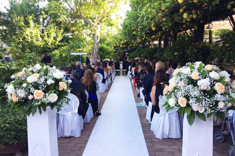Guests seated either side of a white aisle in the garden, with flowers at the head of each row, Villa del Vecchio Pozzo in Posillipo