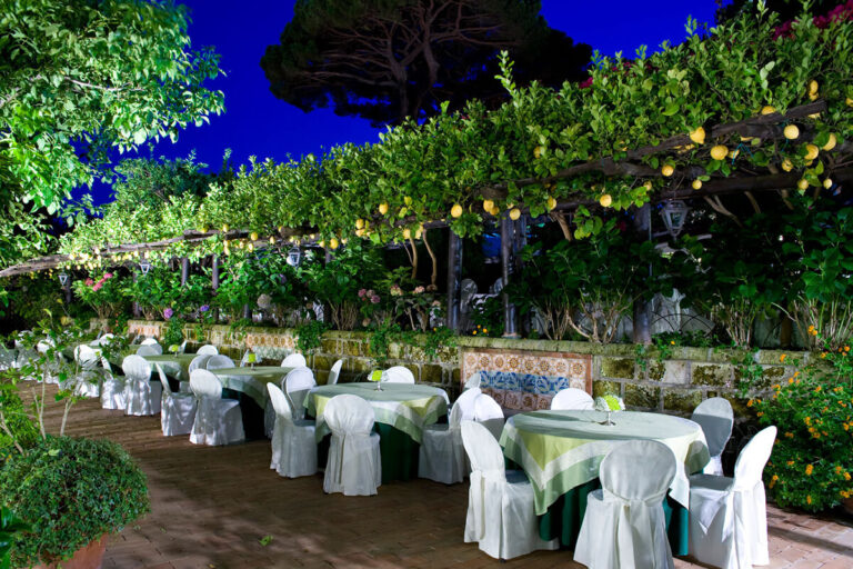 Tables along the lemon pergola at dusk, with ceramic-tiled planters behind, Villa del Vecchio Pozzo in Posillipo