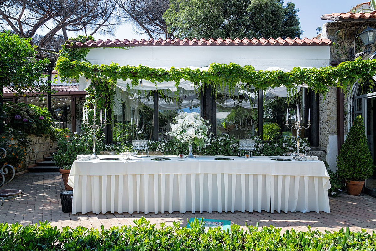 A long table laid under the vine pergola in front of the villa's single-storey garden wing, Villa del Vecchio Pozzo in Posillipo