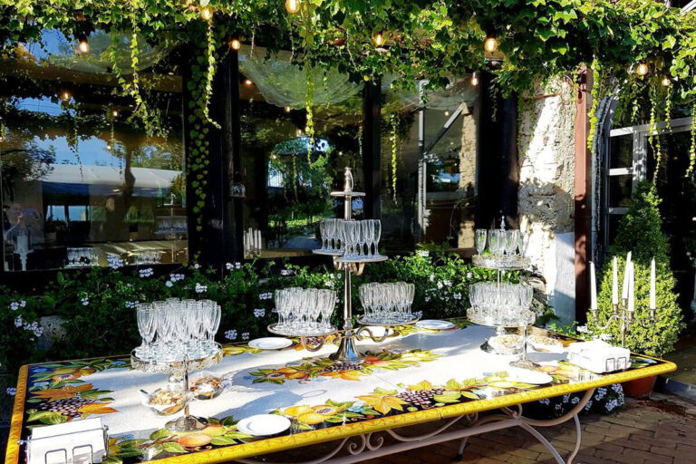 The hand-painted Vietri ceramic table under the pergola, set with glasses and candles, Villa del Vecchio Pozzo in Posillipo