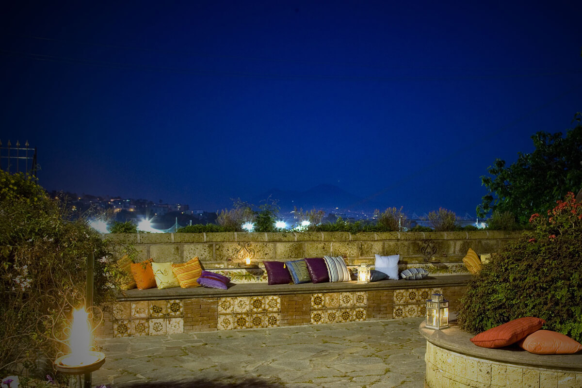 A tiled bench with cushions on a terrace above the city lights at night, Villa del Vecchio Pozzo in Posillipo