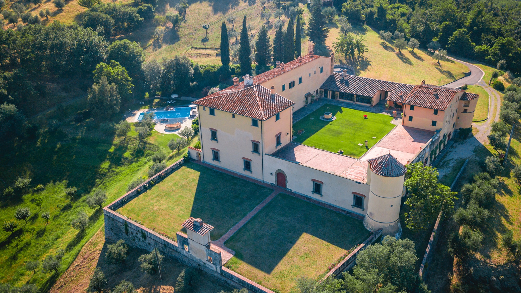 Aerial view of the villa with its square courtyard lawn, corner tower, walled gardens and pool, Villa Il Cerretino