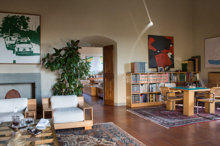 Living room with contemporary art, bookcases, white armchairs and a card table, Villa Il Cerretino