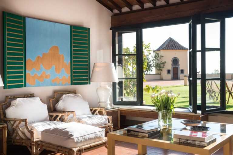 Lounge with bamboo armchairs, a large painting and open windows onto the garden and a small chapel, Villa Il Cerretino